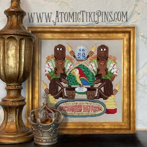 Peut inclure: Une œuvre d'art au point de croix encadrée, représentant un perroquet coloré, des figures tiki et le texte "Enchanted Tiki Room". L'œuvre comprend le nom "JOSE". L'adresse du site Web "WWW.ATOMICTIKIPINS.COM" est affichée en haut.
