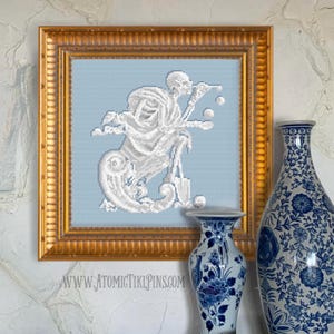 May include: A framed cross-stitch artwork featuring a white skeleton figure on a light blue background. The artwork is in a gold frame and is displayed with two blue and white patterned vases. The website address "WWW.ATOMICTIKIPINS.COM" is visible at the bottom.