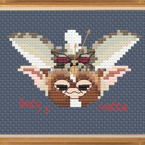 May include: Cross-stitch art of a Gremlin character with large ears and wings, set against a blue background. The artwork includes the text "Baby's" and "Sweet". The piece is framed in a gold-colored wooden frame.