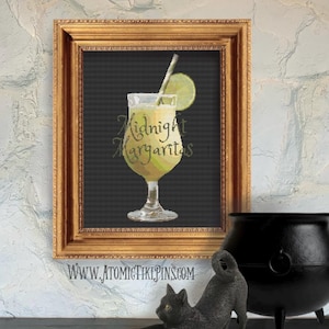 May include: A framed print featuring a cross-stitch design of a margarita cocktail. The drink is in a stemmed glass with a lime wedge and straw. The text "Midnight Margaritas" is written in cursive. The frame is gold.