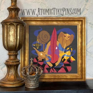 May include: A framed cross-stitch artwork featuring a stylized depiction of characters and objects from a fantasy story. The artwork includes a cobra, a magic lamp, and a genie. The frame is gold-colored, and the background is black.