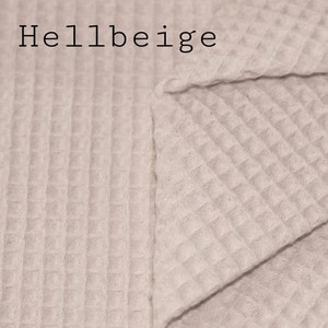 May include: A close-up of a light beige waffle weave fabric. The fabric is folded in half, showing the texture of the weave. The text "Hellbeige" is printed in black at the top of the image.
