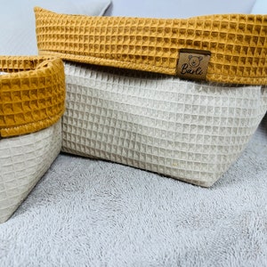 May include: Two waffle-textured storage baskets with brown trim and a brown bear logo that says "B&auml;rli". The baskets are on a light gray fuzzy surface.