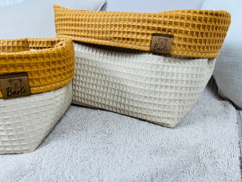 May include: Two waffle-textured storage baskets with brown trim and a brown bear logo that says "B&auml;rli". The baskets are on a light gray fuzzy surface.