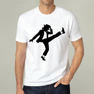 Puede incluir: Camiseta blanca con una silueta negra de una persona con traje y sombrero, realizando un movimiento de baile con una pierna levantada. El dise&ntilde;o es una representaci&oacute;n gr&aacute;fica de una famosa pose de baile.