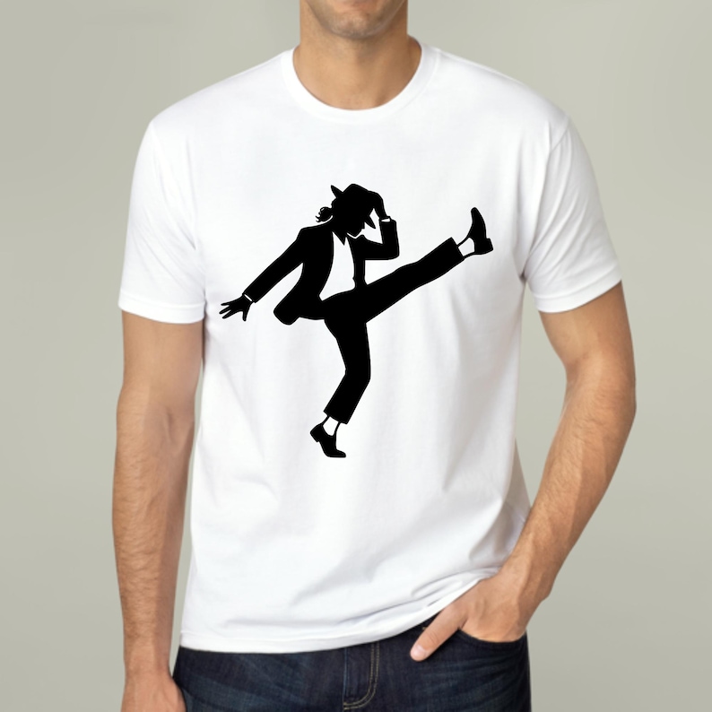 Puede incluir: Camiseta blanca con una silueta negra de una persona con traje y sombrero, realizando un movimiento de baile con una pierna levantada. El dise&ntilde;o es una representaci&oacute;n gr&aacute;fica de una famosa pose de baile.