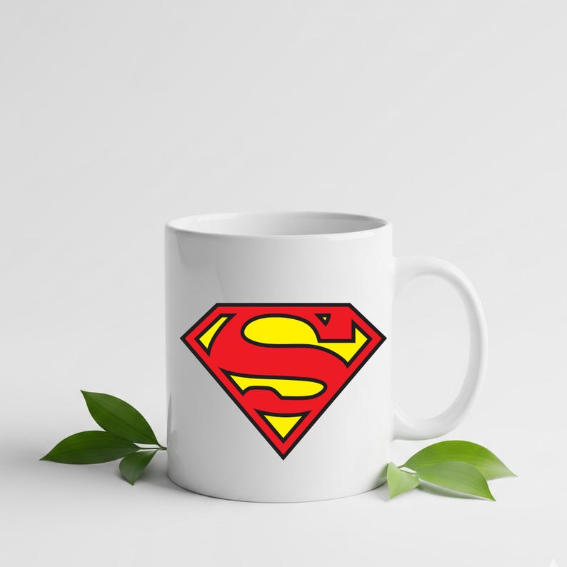 May include: White ceramic mug featuring the iconic Superman logo. The logo is a red diamond shape with a yellow 'S' inside, outlined in black. The mug has a curved handle and is suitable for hot or cold beverages.