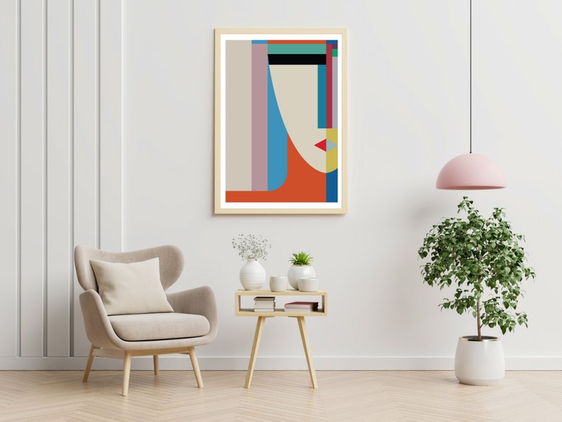 May include: Abstract geometric art print with a stylized face in shades of blue, red, yellow, and green. The print is framed in a light wood frame and is hanging on a white wall.