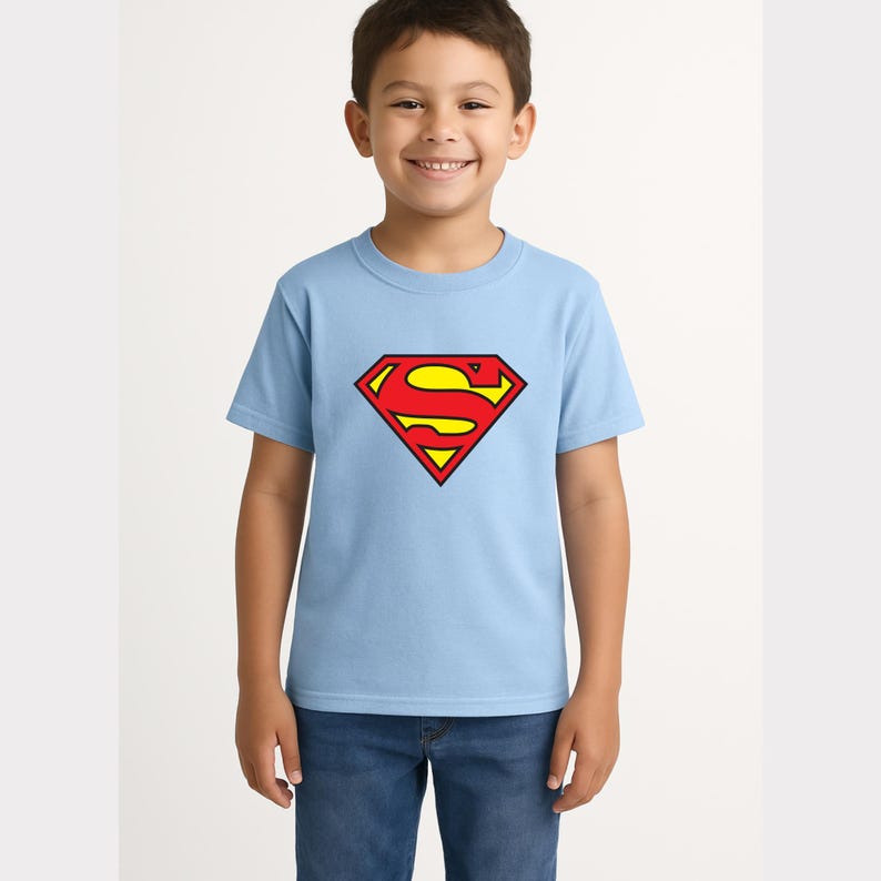 May include: A light blue t-shirt featuring the Superman logo in red and yellow. The logo is a diamond shape with the letter "S" in the center. The shirt is short-sleeved and made of a soft material.
