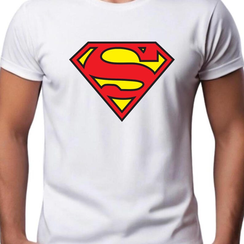 May include: White t-shirt featuring the iconic Superman logo. The logo is a red diamond shape with a yellow center and black outline. The shirt is a classic crew neck style.