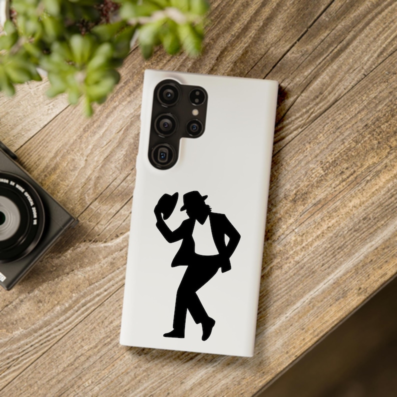 Puede incluir: Una funda de tel&eacute;fono blanca con una silueta negra de una persona con sombrero, en pose de baile. El dise&ntilde;o incluye un traje negro, camisa blanca y sombrero. La funda tiene un m&oacute;dulo de c&aacute;mara en la parte superior.