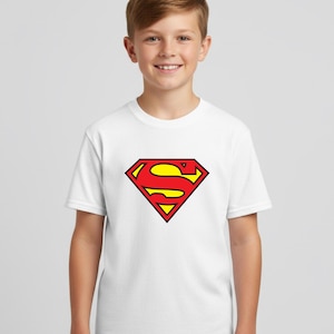 May include: White t-shirt featuring the Superman logo. The logo is a red and yellow diamond shape with a stylized "S" in the center. The shirt is short-sleeved and appears to be made of cotton.