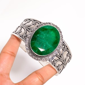 Puede incluir: Brazalete de puño plateado con una piedra preciosa verde esmeralda de corte ovalado. El brazalete presenta intrincados diseños de filigrana en espiral a lo largo de la banda y alrededor de la piedra preciosa. Una joya clásica.