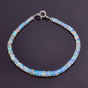 Op de afbeelding: Een delicate armband bestaande uit kleine, iriserende opaal kralen. De kralen vertonen een reeks kleuren, waaronder blauw, groen en geel, geregen met een zilveren sluiting. De armband is ontworpen om om de pols te worden gedragen.