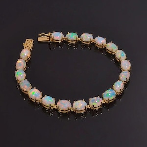 May include: A gold bracelet featuring oval-shaped opals. Each opal is set in a gold bezel and linked together. The opals display a play of color, with flashes of green, blue, and yellow. The bracelet is secured with a gold clasp.
