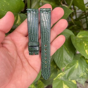 May include: Two green watch straps made of lizard skin. The straps are both about 18 cm long and 2 cm wide. The straps have a textured surface and a pointed end.