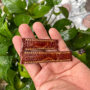 May include: Two brown leather watch straps with yellow stitching. The straps are made of a textured material that resembles alligator skin.