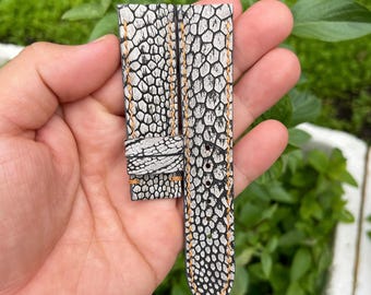Könnte beinhalten: Ein weiß-schwarzes Uhrenarmband mit einem strukturierten Muster und orangefarbenen Nähten. Das Armband ist aus Leder und hat ein spitz zulaufendes Ende.
