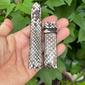 Könnte beinhalten: Zwei Uhrenarmbänder aus weißem und braunem Schlangenleder mit einem hellbraunen Nähten-Detail.