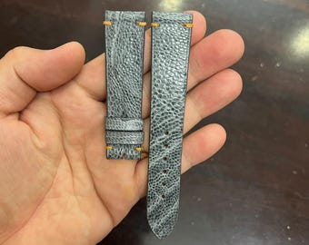 Könnte beinhalten: Graues Lederarmband mit orangefarbener Naht. Das Armband hat eine strukturierte Oberfläche und ist für eine Armbanduhr konzipiert.