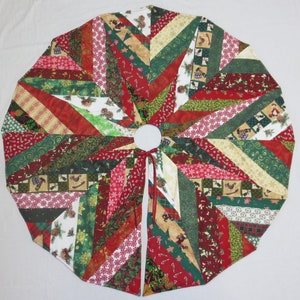 May include: A Christmas tree skirt with a patchwork design. The skirt features a variety of fabrics in red, green, and white, with patterns including candy canes, snowflakes, and pinecones. The skirt has a circular shape with a center opening and ties.