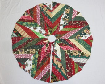 May include: A Christmas tree skirt with a patchwork design. The skirt features a variety of fabrics in red, green, and white, with patterns including candy canes, snowflakes, and pinecones. The skirt has a circular shape with a center opening and ties.