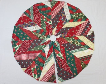 May include: Circular Christmas tree skirt with a patchwork design. The skirt features red, green, and white fabrics with holiday patterns like poinsettias, candy canes, and plaid. The center has a white circle and a split opening.