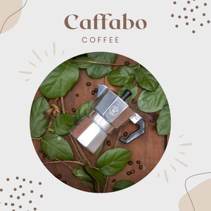 Könnte beinhalten: Eine silberne Kaffeemaschine mit schwarzem Griff, umgeben von grünen Blättern und Kaffeebohnen auf einer Holzoberfläche. Der Text "Caffabo COFFEE" wird über der Kaffeemaschine angezeigt.