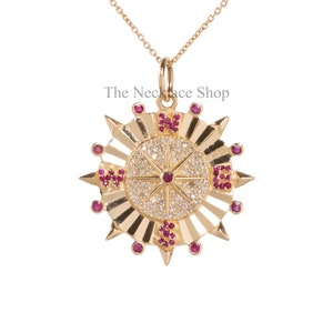 May include: Gold compass pendant necklace with a diamond-encrusted centre and ruby accents. The compass points north, south, east, and west. The necklace is on a delicate gold chain.
