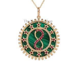May include: Gold pendant necklace featuring a green malachite stone, a ruby infinity symbol, and a circle of stars and diamonds. The pendant is attached to a gold chain.