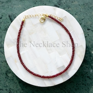 May include: A delicate red gemstone necklace with a gold clasp. The necklace is made of small, faceted beads and is displayed on a white background.