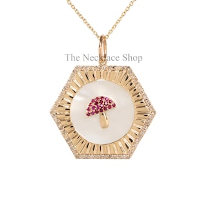 Könnte beinhalten: Goldkette mit einem sechseckigen Anhänger mit einer weißen Perlmutteinlage und einem roten Rubin-Pilz-Design. Der Anhänger ist von einem Rand aus kleinen Diamanten umgeben. Die Kette ist von The Necklace Shop.