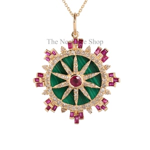 May include: Gold pendant necklace featuring a circular design with a green malachite center and a ruby gemstone. The pendant is adorned with diamonds and ruby accents, suspended from a delicate gold chain. The text "The Necklace Shop" is visible.