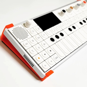 Puede incluir: Un teclado de música electrónico blanco y naranja con una pequeña pantalla y una variedad de botones y perillas. El teclado tiene un altavoz incorporado y un soporte.