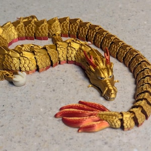 May include: A gold and red segmented dragon toy with a detailed head and a long tail. The dragon is made of plastic and has a segmented body that allows it to bend and move.