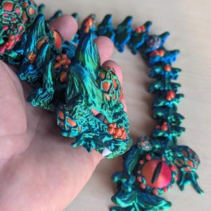 May include: A green and orange dragon necklace with red eyes. The necklace is made of plastic and is about 18 inches long.