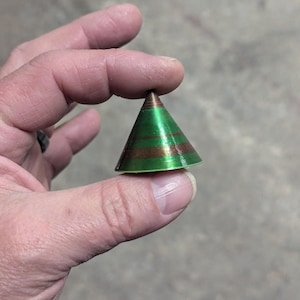 May include: A small, green, cone-shaped ornament with gold stripes. The ornament is made of a shiny material and has a pointed tip.