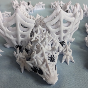 May include: A group of white, spider-shaped figurines with black accents. The figurines are made of a plastic-like material and have a detailed, intricate design.