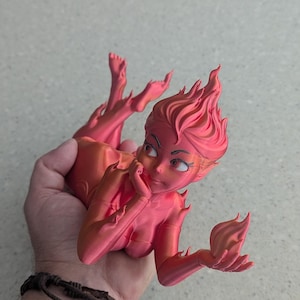 May include: A 3D-printed figurine of a stylized female figure with fiery hair and limbs, in shades of pink and orange. The figure is posed with a hand to the face, and the other hand holding a flame-like shape.