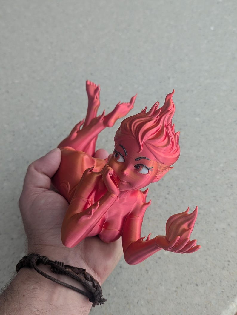 May include: A 3D-printed figurine of a stylized female figure with fiery hair and limbs, in shades of pink and orange. The figure is posed with a hand to the face, and the other hand holding a flame-like shape.