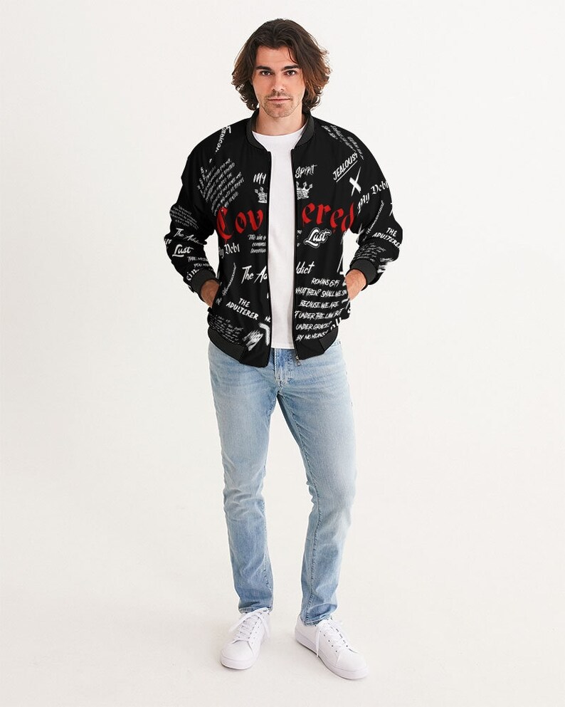 May include: A black bomber jacket with a white and red print. The print includes the words "Covered" and "Lust" in red. The jacket has a zipper closure and two pockets.