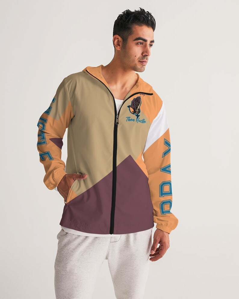 May include: A beige, orange, white and maroon windbreaker jacket with a black zip. The jacket has a graphic of a praying hand with the text "Then Hustle" on the left side and the text "Pray" on the right side.