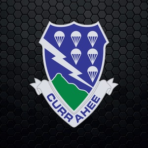 Puede incluir: Un escudo azul con un rayo y seis paracaídas. El escudo está rodeado por una montaña verde y una cinta blanca con el texto "CURRAHEE".