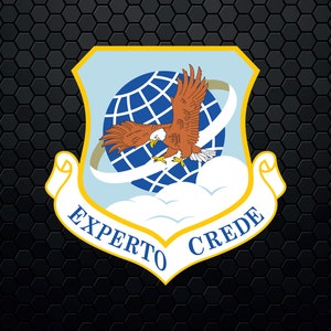 May include: A blue and white shield with a yellow border and a scroll at the bottom. The shield features a globe with a red-tailed hawk flying around it. The scroll reads "Experto Crede".