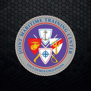 Puede incluir: Un sello circular con el texto "Joint Maritime Training Center" en un borde de cuerda gris. El sello tiene un fondo morado con cuatro escudos, una brújula y dos espadas cruzadas. Los escudos presentan un águila roja, blanca y azul, un tridente, una brújula y un ancla. El texto "Unus Humus Unus Pugna" está en la parte inferior del sello.