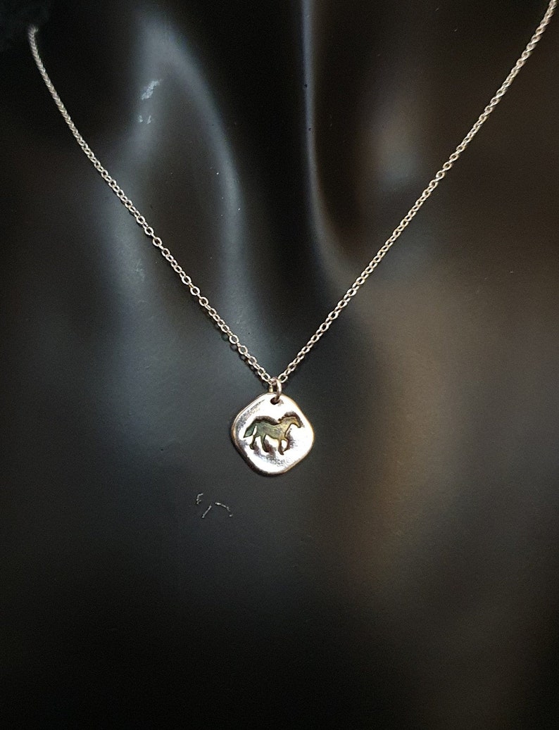 May include: A silver chain necklace with a silver pendant featuring a horse silhouette.