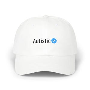 以下が含まれることがあります： 黒い文字で「Autistic」と書かれ、その後に青い認証済みチェックマークアイコンが付いた白い野球帽。この帽子は構造化されたクラウン、湾曲したつば、上部のボタンが特徴で、シンプルで清潔感のあるデザインに仕上がっています。
