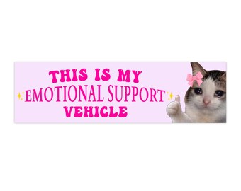 Puede incluir: Una pegatina rectangular con fondo rosa claro y el texto en rosa intenso THIS IS MY EMOTIONAL SUPPORT VEHICLE. A la derecha, un gato blanco y marrón con un lazo rosa en la cabeza aparece haciendo un gesto de pulgar hacia arriba.