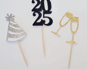 May include: Three cupcake toppers for a New Year's Eve party. One topper is a black glitter 2025, another is a silver glitter party hat, and the last is two gold glitter champagne glasses.