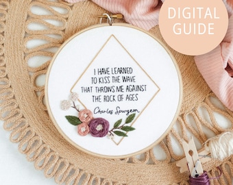 May include: Embroidered hoop art with a quote by Charles Spurgeon: "I have learned to kiss the wave that throws me against the rock of ages." The quote is surrounded by a floral design with pink and purple flowers.